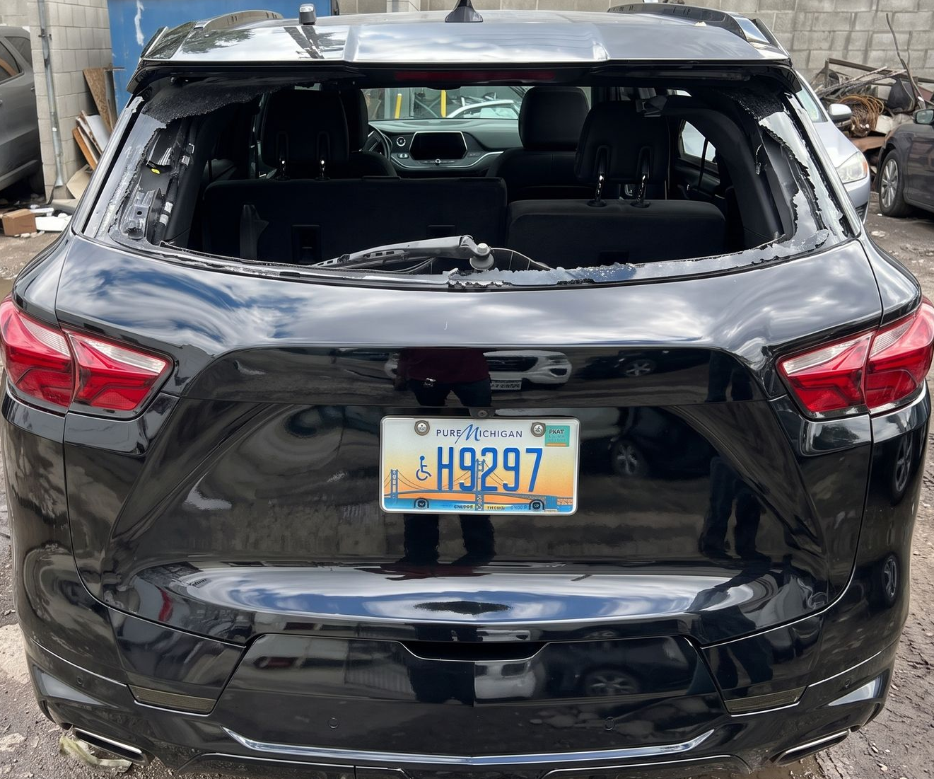 Damaged black SUV with shattered rear window and a license plate, parked outdoors among debris