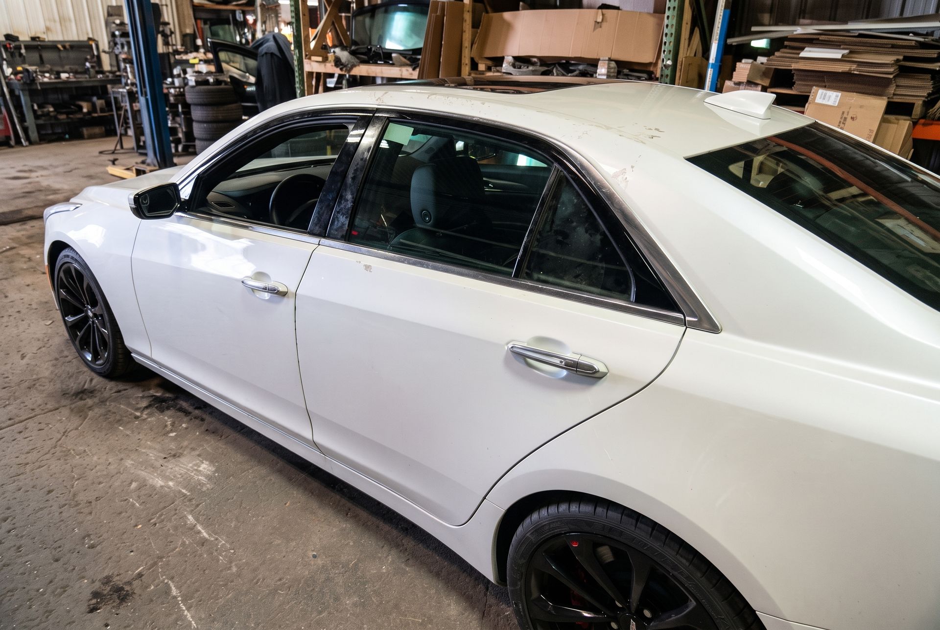 White sedan in a workshop garage, viewed from the side with black wheels.