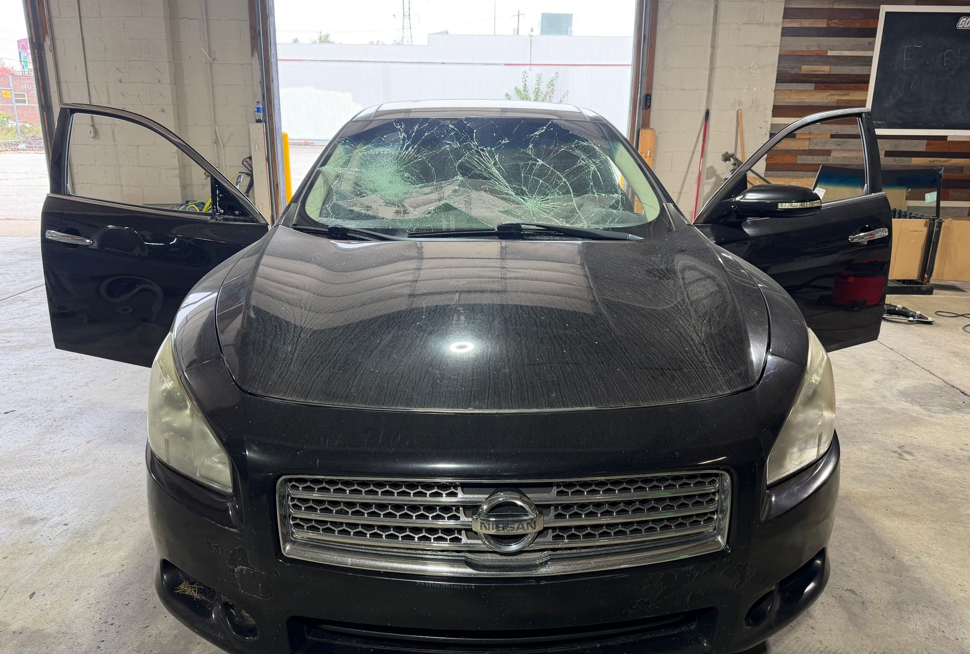 Damaged black SUV with shattered rear window and a license plate, parked outdoors among debris