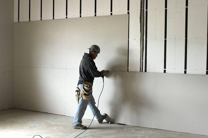 Worker using a drywall sander on a partially finished interior wall