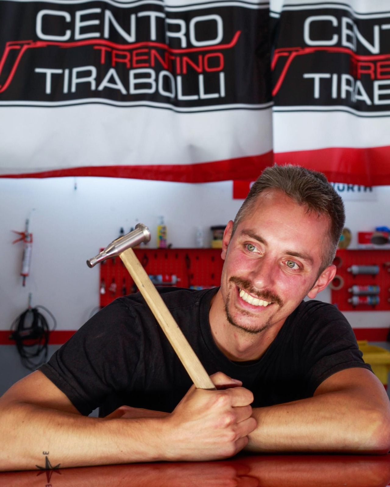 Un uomo che tiene un martello davanti a un cartello che dice centro trentino tirabolli