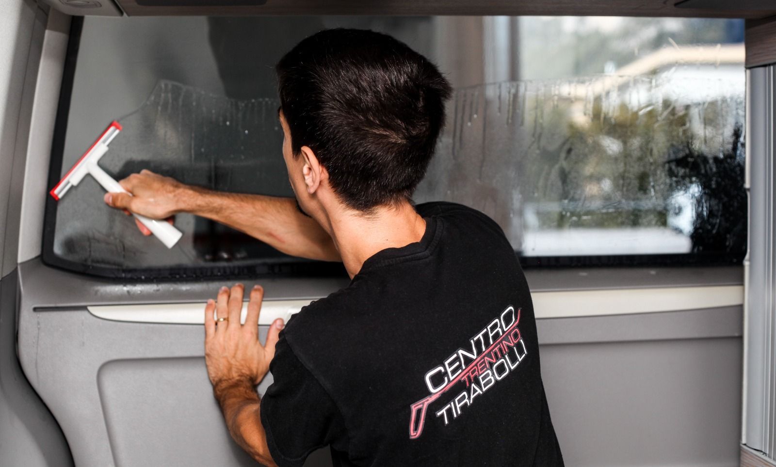 Un uomo sta pulendo il lunotto posteriore di un furgone con un tergivetro.