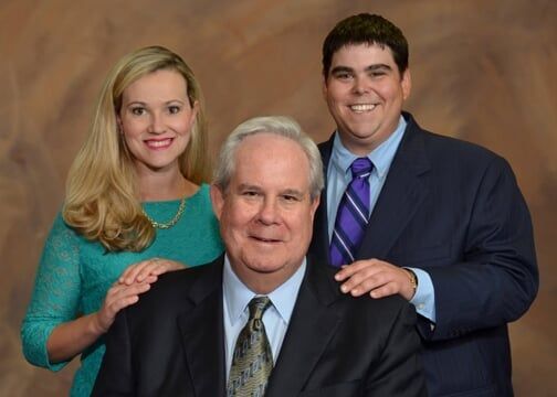 A man in a suit and tie is posing for a picture with his wife and son.