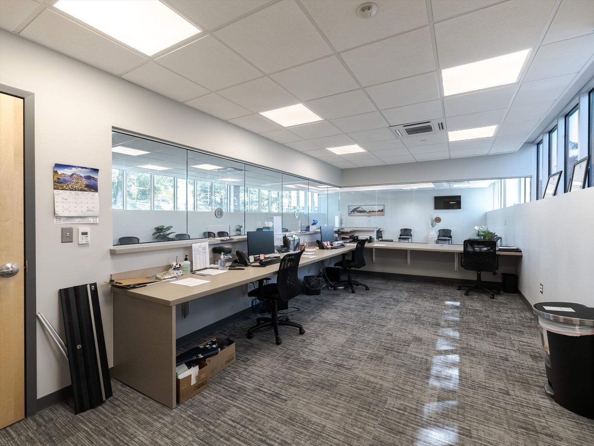 Empty modern office with desks, computer monitors, chairs, and large windows under bright ceiling lights Empty modern office with desks, computer monitors, chairs, and large windows under bright ceiling lights