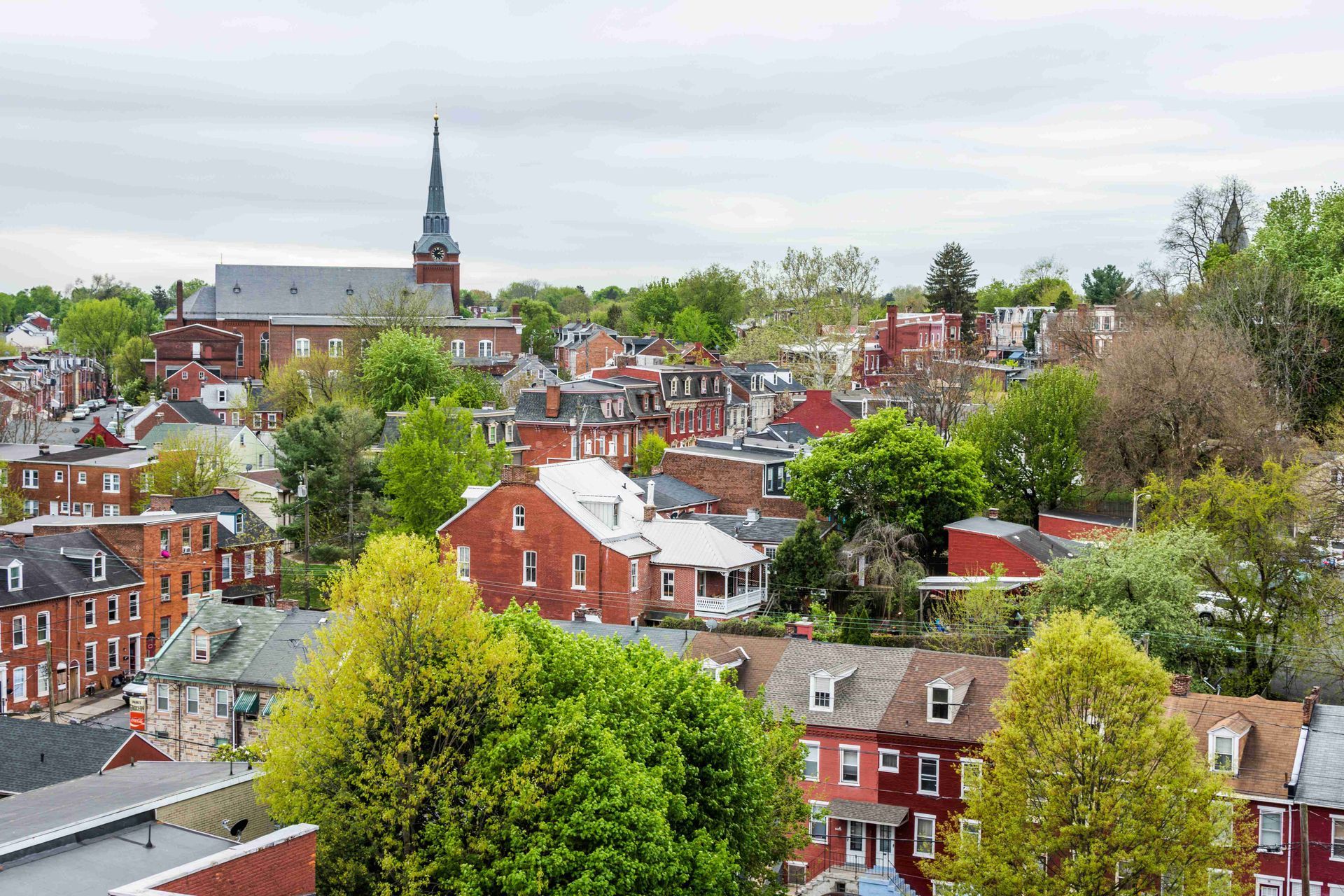 Aerial view of a red-brick town with trees and a church steeple under an overcast sky