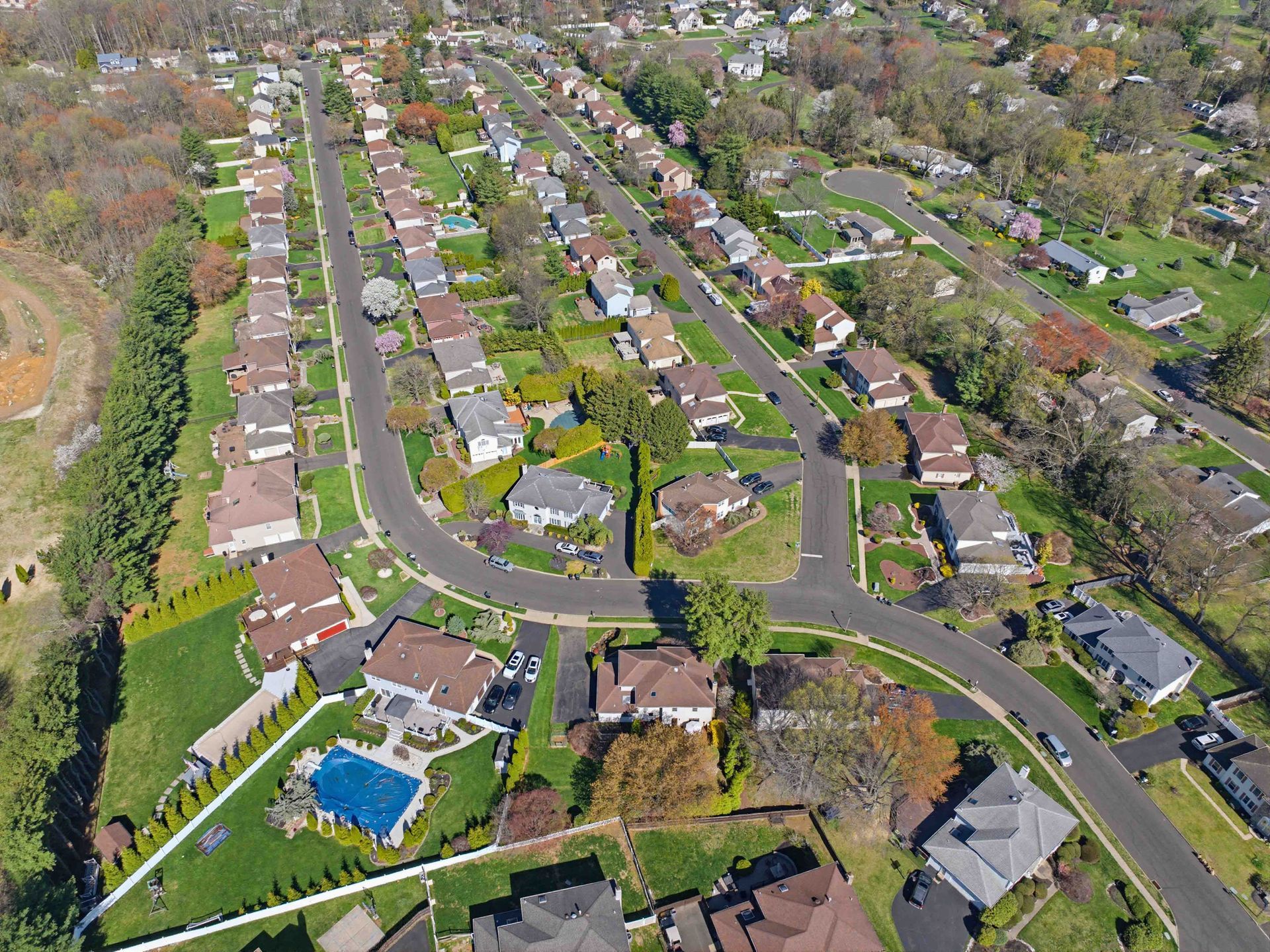 Aerial view of a suburban neighborhood with curved streets, houses, trees, and a backyard pool.