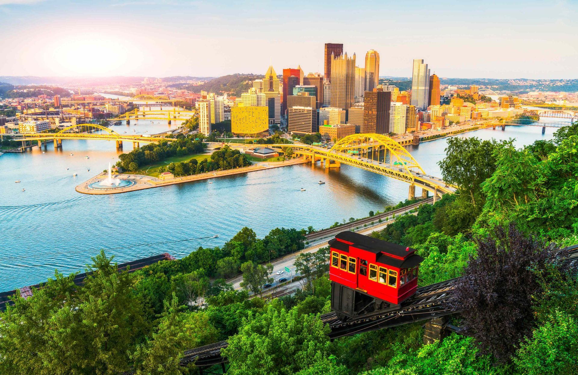 Sydney skyline and harbor with a red funicular climbing a green hillside at sunset
