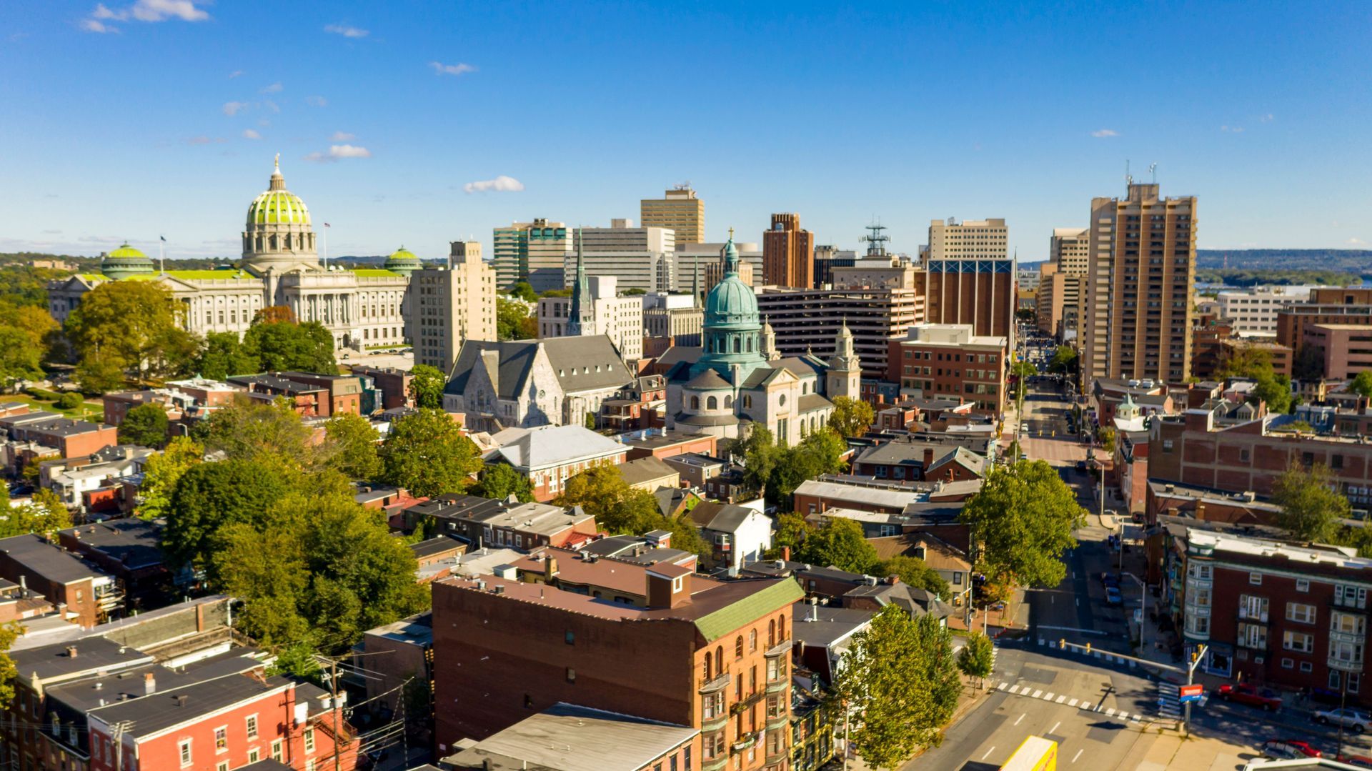 Downtown city skyline with historic domed building, modern high-rises, and tree-lined streets under a blue sky