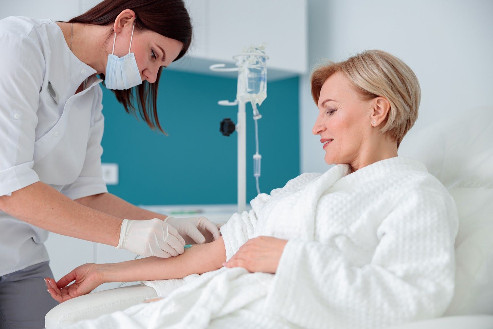 Nurse checking a patient’s arm in a hospital bed beside an IV stand