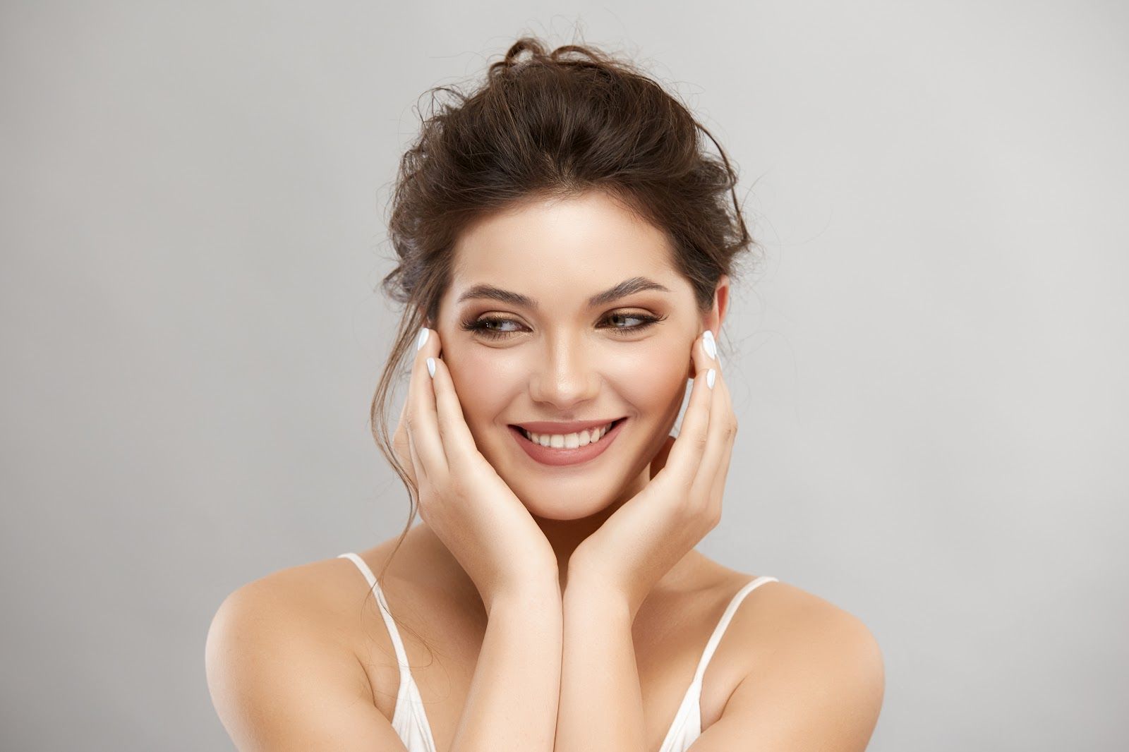 Smiling woman touching her face against a light gray background