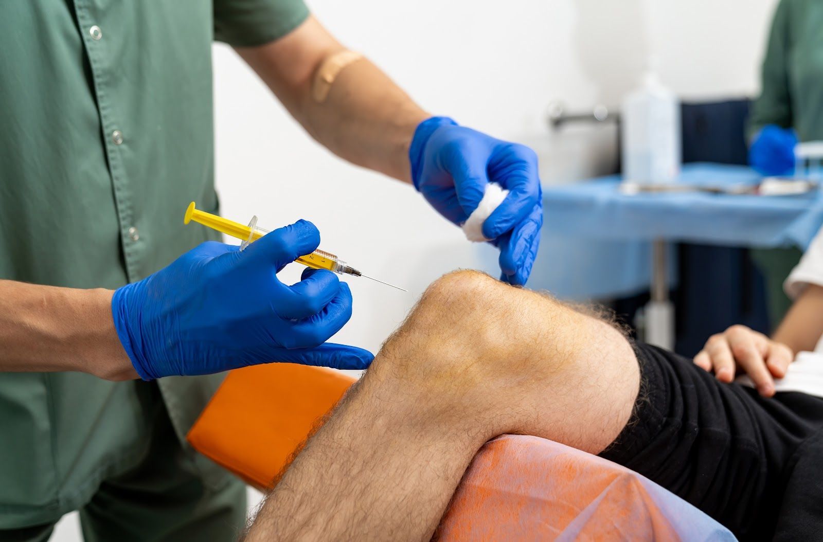 Medical professional bandaging a patient’s knee with blue gloves in a clinic setting