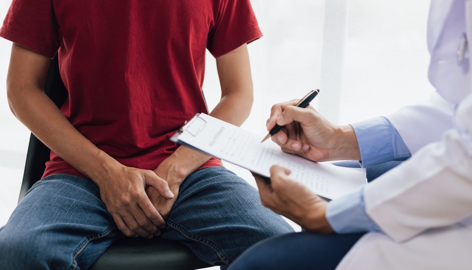 Patient seated beside doctor writing notes on a clipboard during a medical consultation