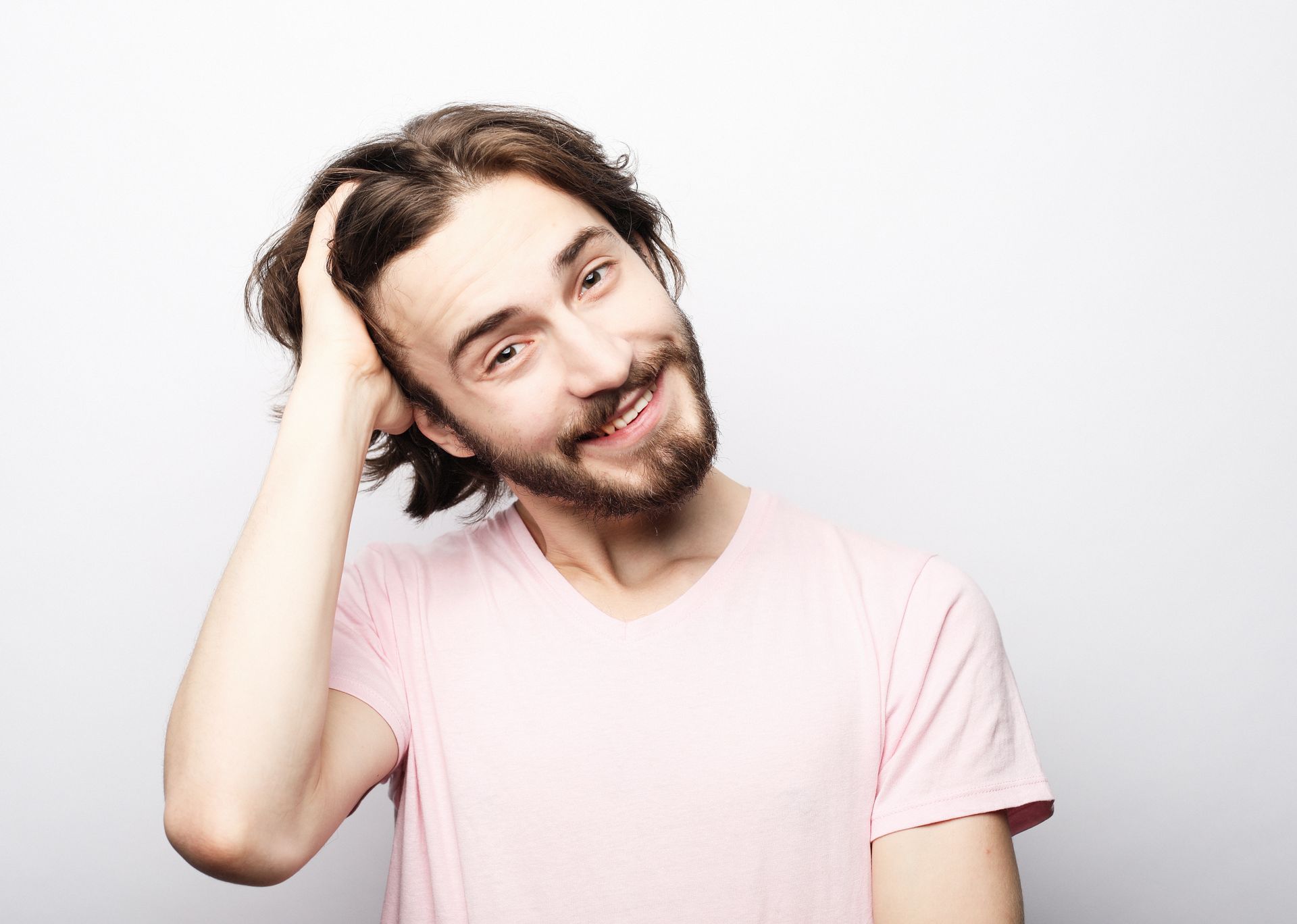 Smiling person in a light pink shirt tilting head and touching hair against a white background