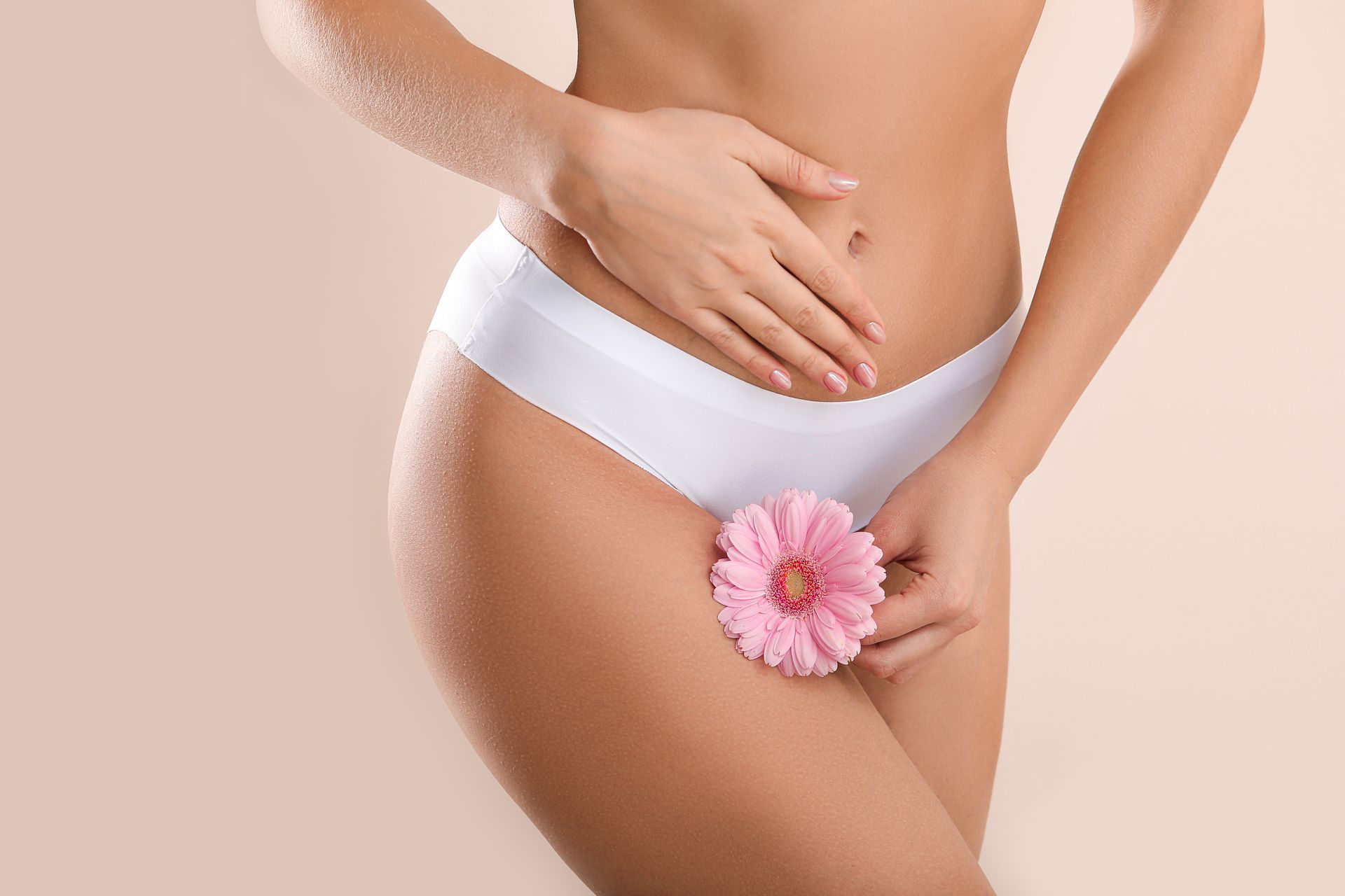 Woman in white underwear, hand on stomach, holding pink flower over pubic area.