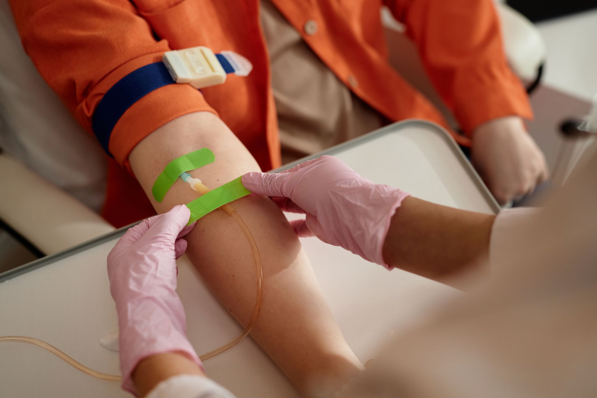 Healthcare worker drawing blood from a patient’s arm with pink gloves and green tape on a clinic chair