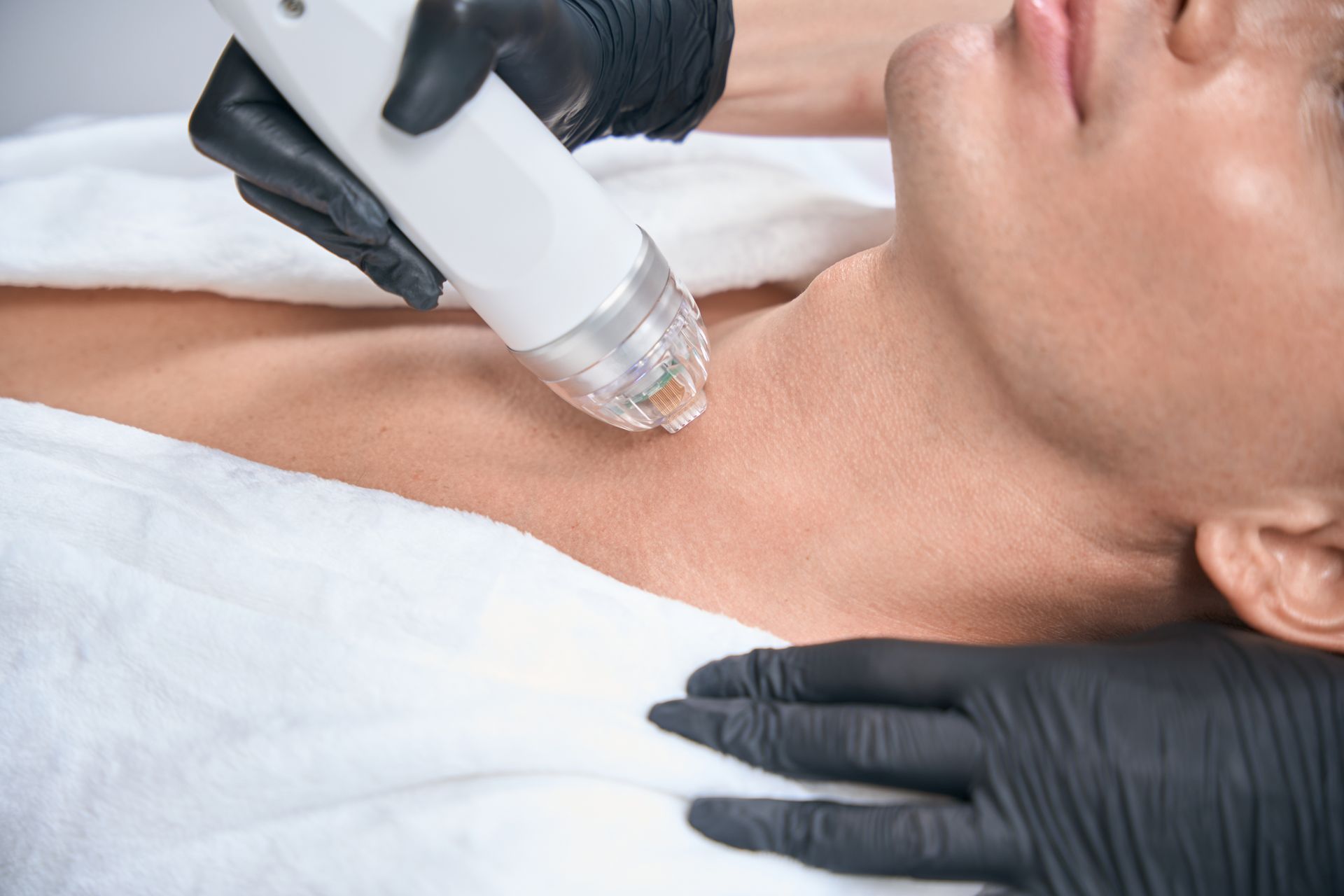 Gloved hands using a facial treatment device on a person’s neck and chest in a spa setting