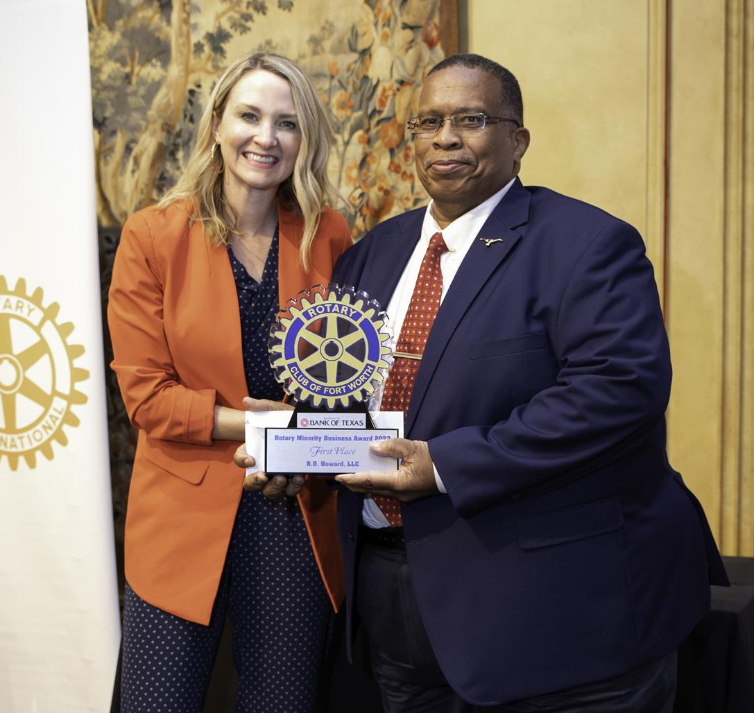 Woman in orange blazer presents award to man in blue suit. Rotary Club logo.