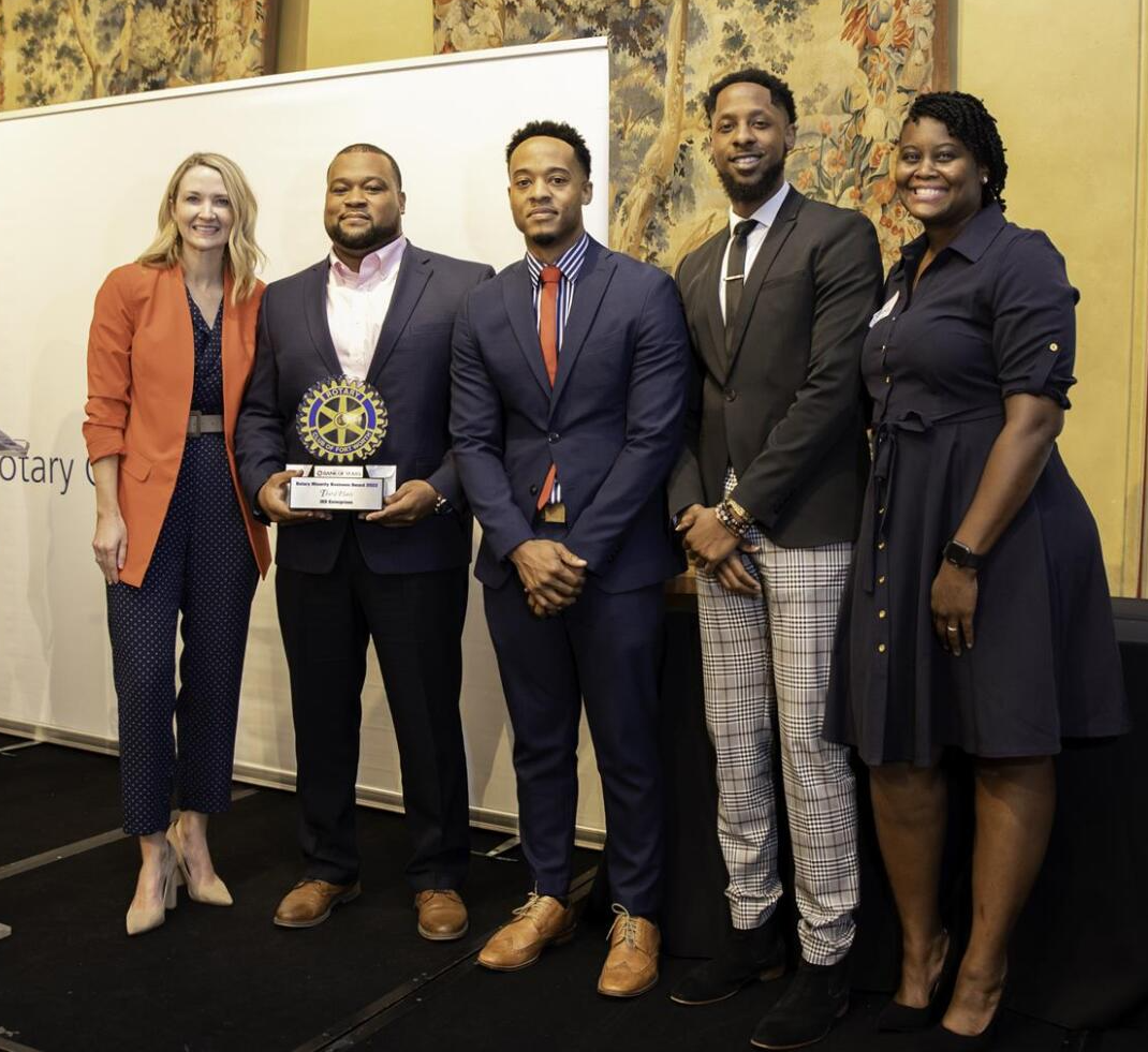 Group of people holding an award, standing on a stage. They are dressed in formal attire in front of a white backdrop.