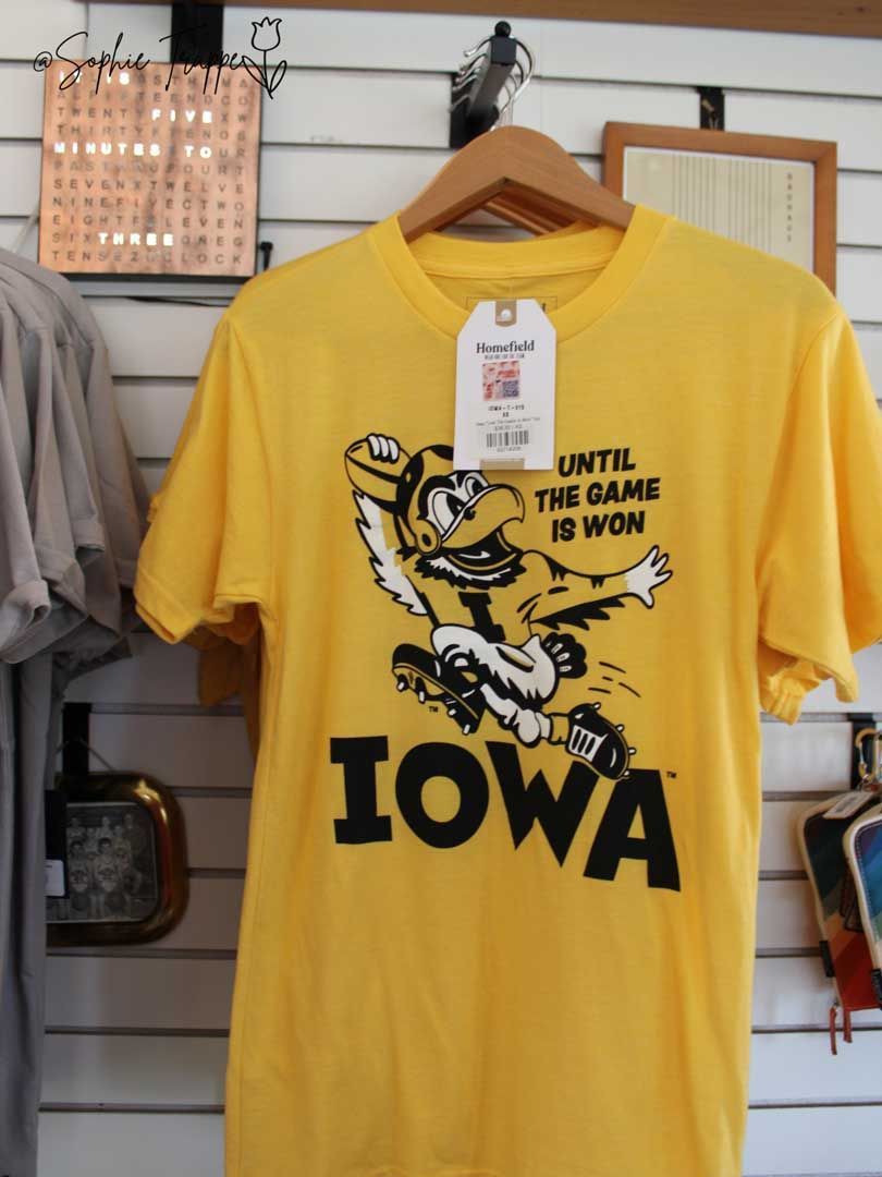Yellow Iowa Hawkeyes T-shirt with mascot and “Iowa” text hanging on a display wall