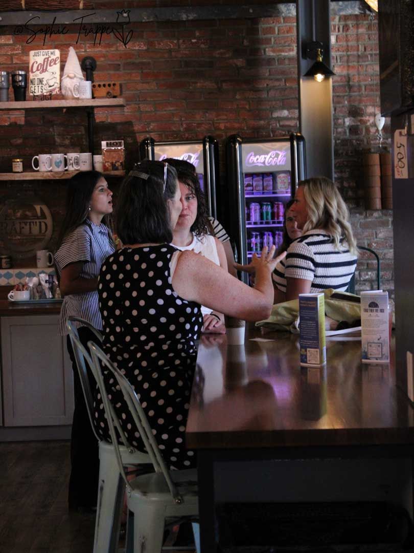 People seated at a café table in a dim brick-walled bar or restaurant, chatting with drinks and menus.