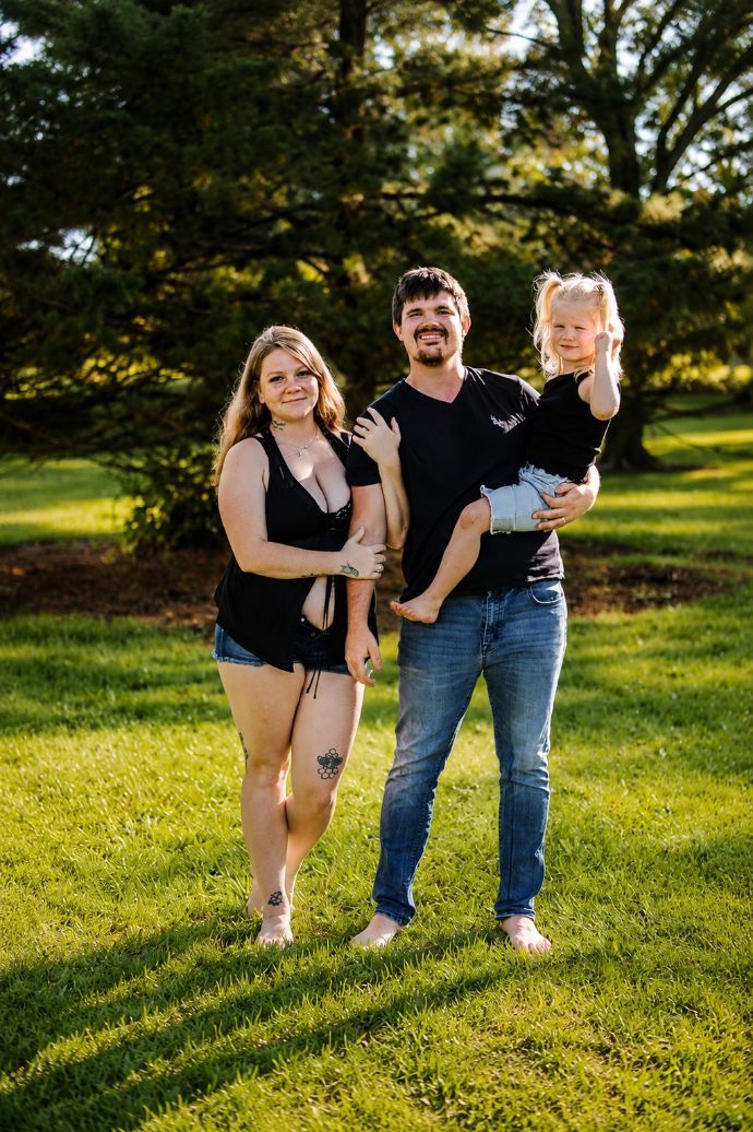 Three people smiling and posing on a grassy field with trees in the background.