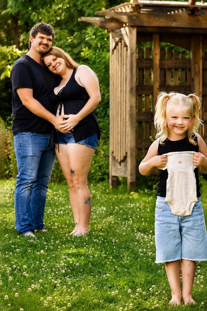 Two adults hugging in a grassy garden while a child stands in front holding a small object
