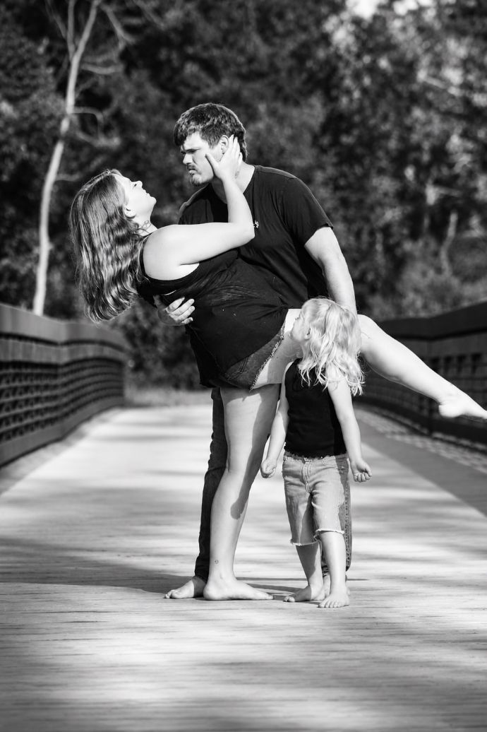 Couple dancing with a child on a tree-lined path, black-and-white photo.