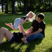Three people relaxing on grass in a sunny park, one child leaning toward the others.
