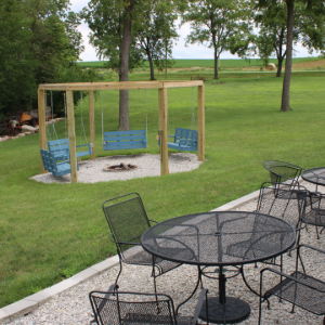 Backyard patio with black metal tables, chairs, and a fenced sand play area near a grassy field