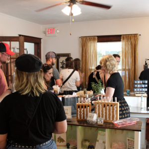 People browsing products at a small indoor market with tables and shelves of jars and bottled goods