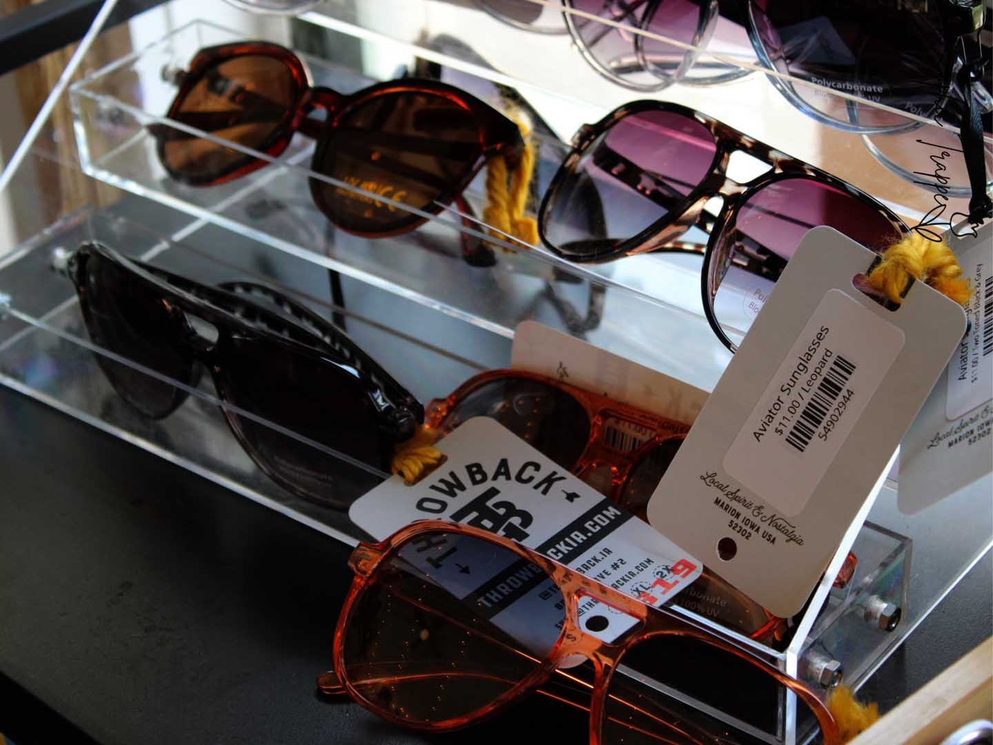 Sunglasses displayed on a glass shelf, including brown, pink, and orange-framed pairs with price tags.