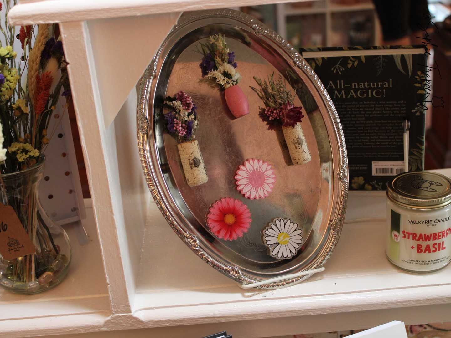 Decorative oval mirror with small hanging charms and flowers on a white shelf beside a strawberry-basil jar