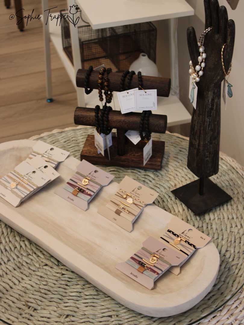 Handmade jewelry displayed on stands and trays on a woven mat in a shop or market setting