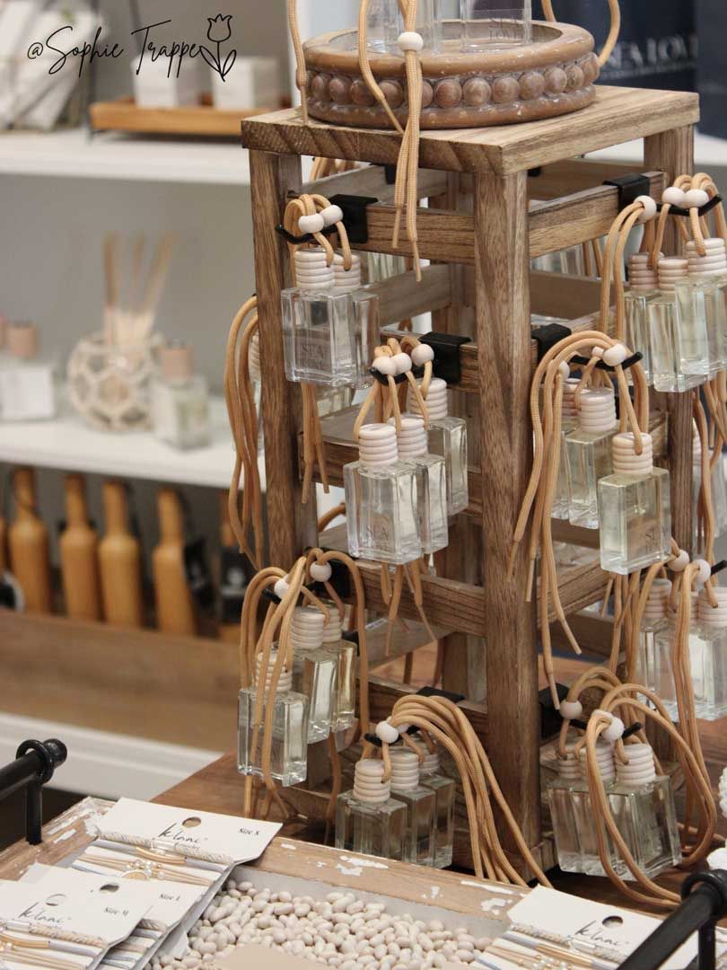 Rustic wooden display stand with small glass bottles and hanging twine-wrapped jars in a shop.