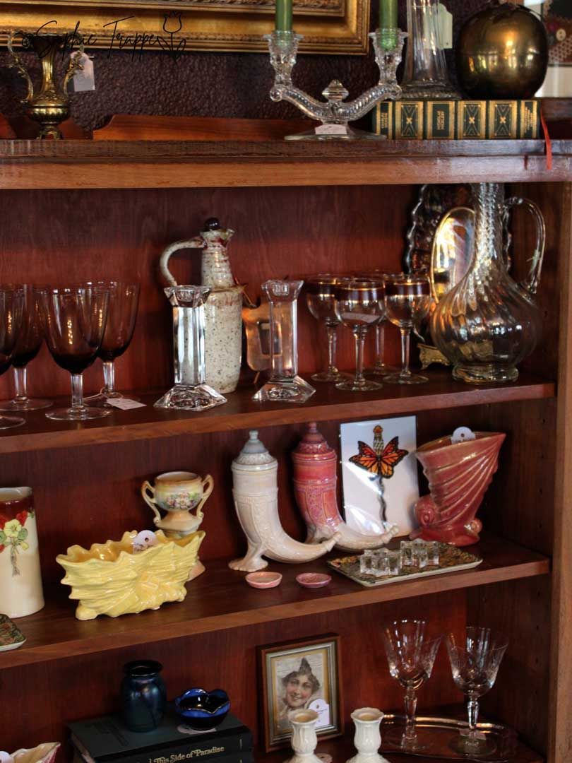 Wooden shelf displaying assorted glassware, vases, and decorative figurines in a home interior.