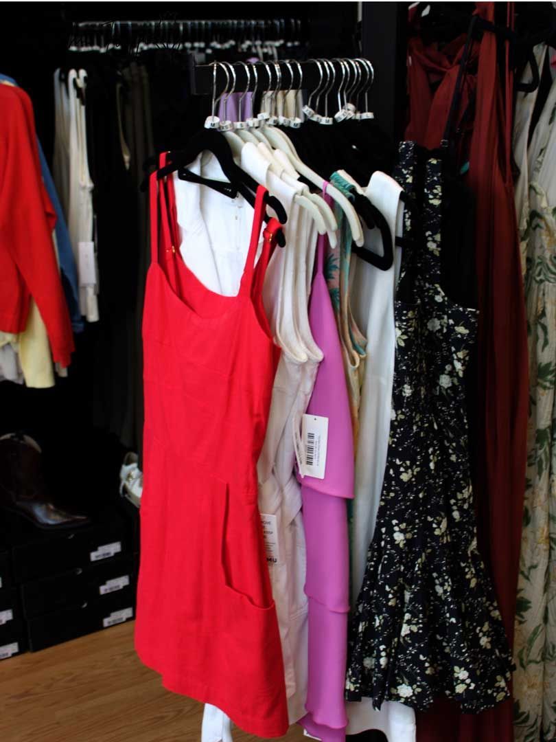 Clothing rack with dresses, including a red dress, pink dress, and black floral dress in a store.