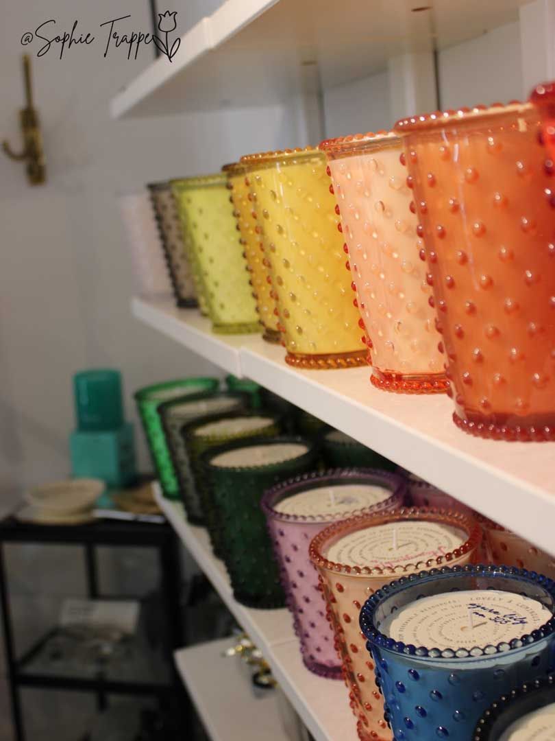 Colorful glass candle holders lined on white shelves in a cozy shop or home display.