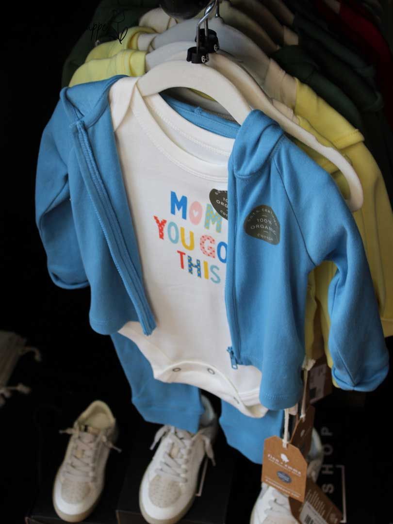 Baby blue hooded onesie on a hanger with a white graphic shirt, in a clothing store display.