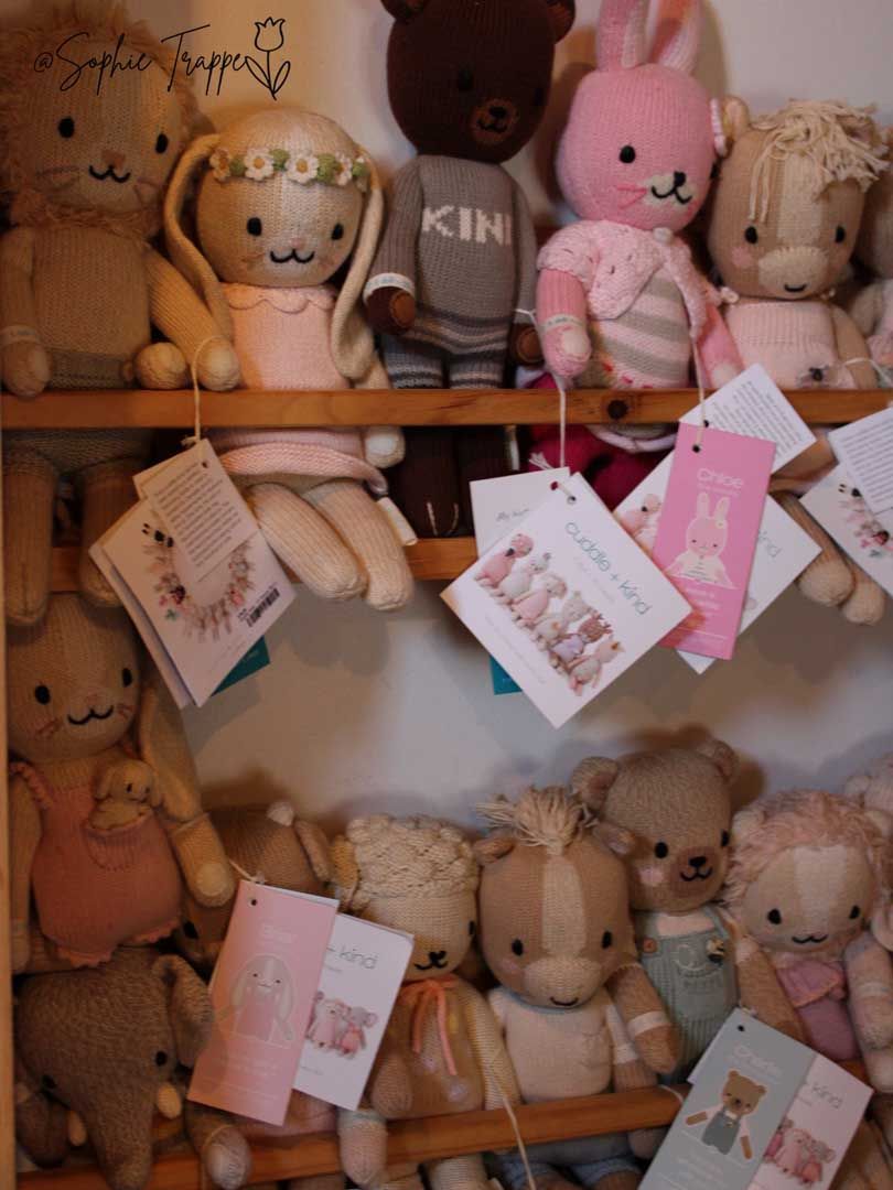 Plush teddy bears and dolls on wooden shelves with hanging pink gift tags in a shop display