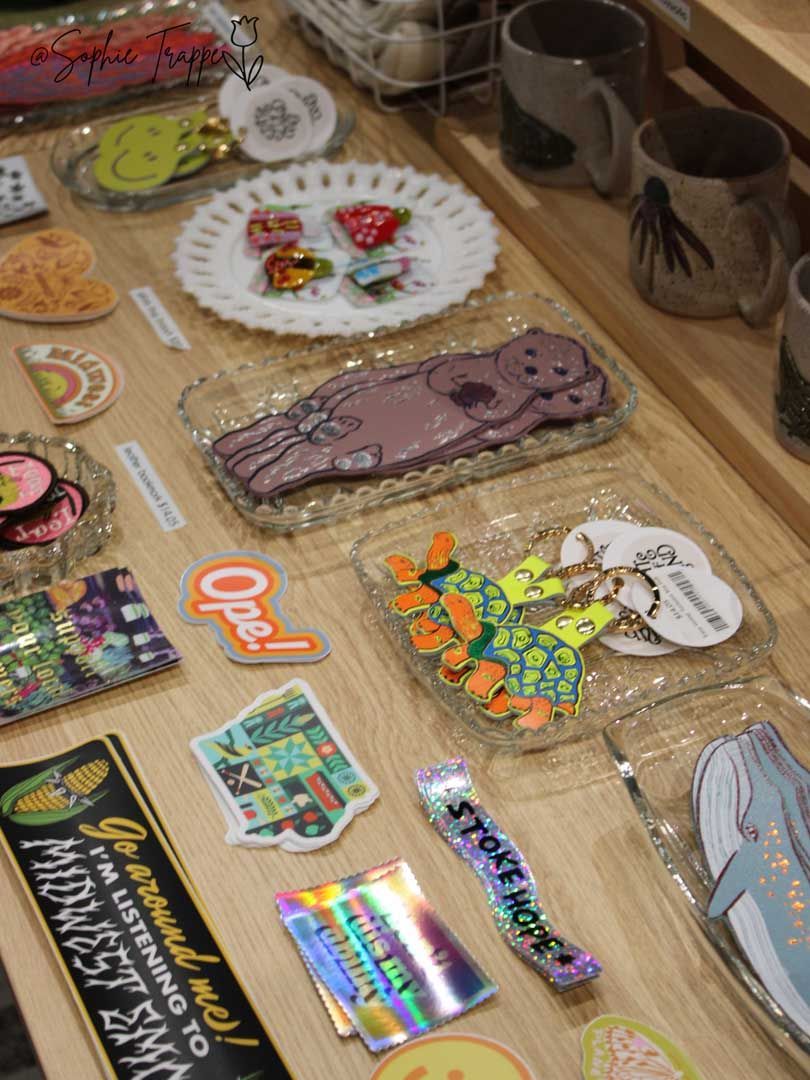 Assorted colorful enamel pins and keychains displayed on a wooden table at a market stall