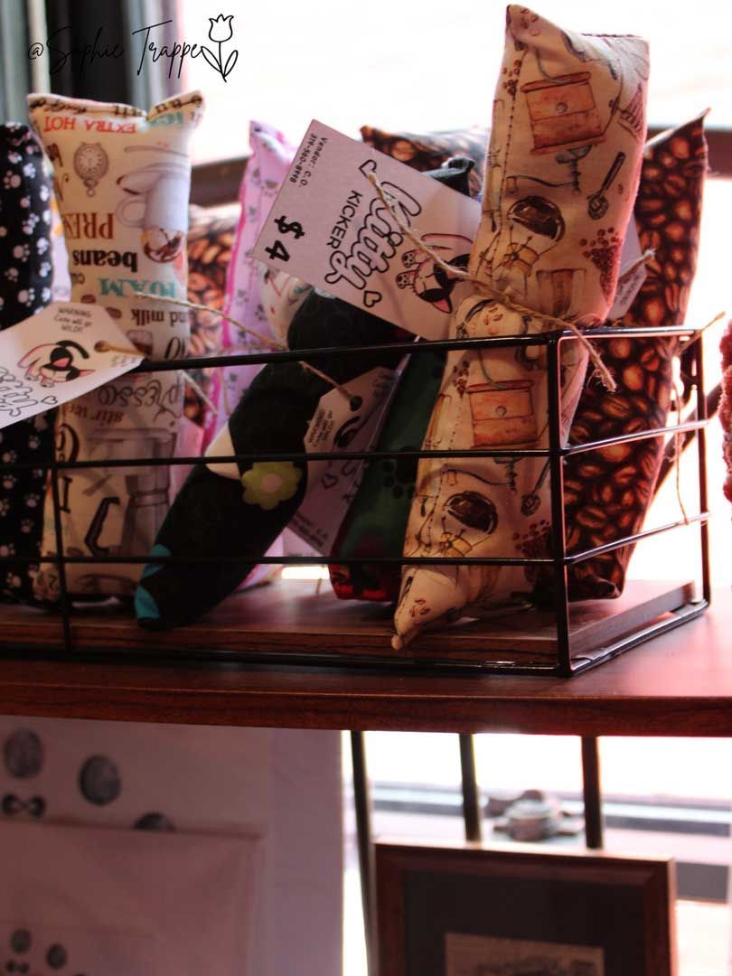 Wire basket of patterned gift bags on a shelf, lit by warm sunlight.