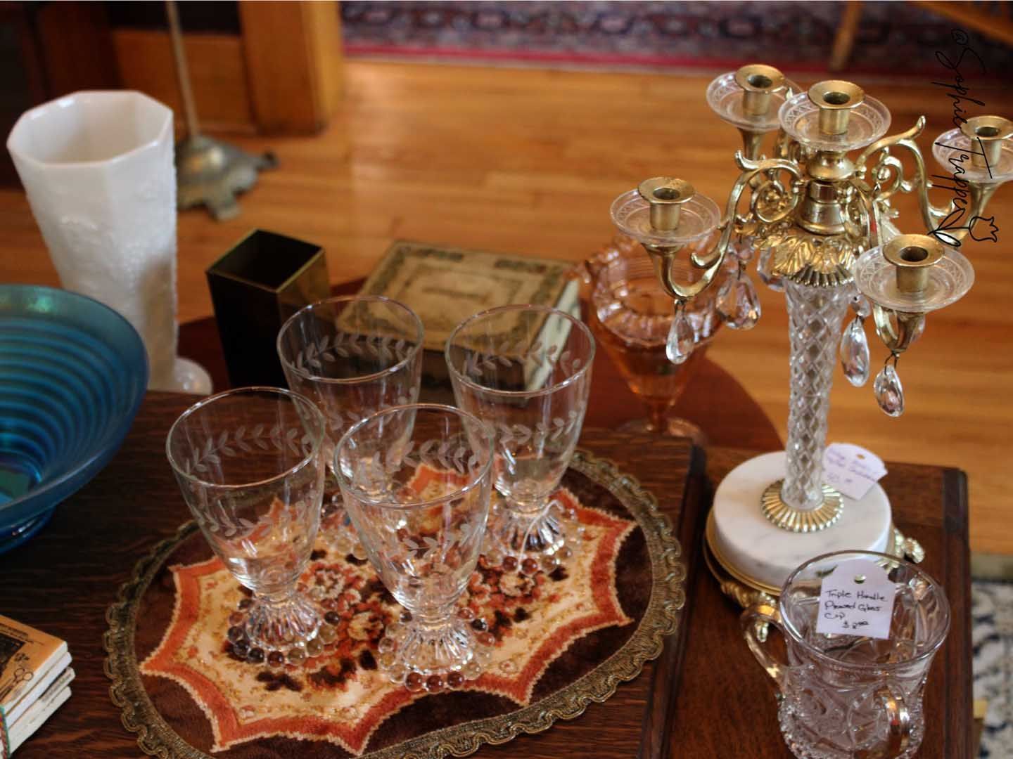 Crystal glasses on a decorative tray beside a gold candelabra and a blue bowl on a wooden table