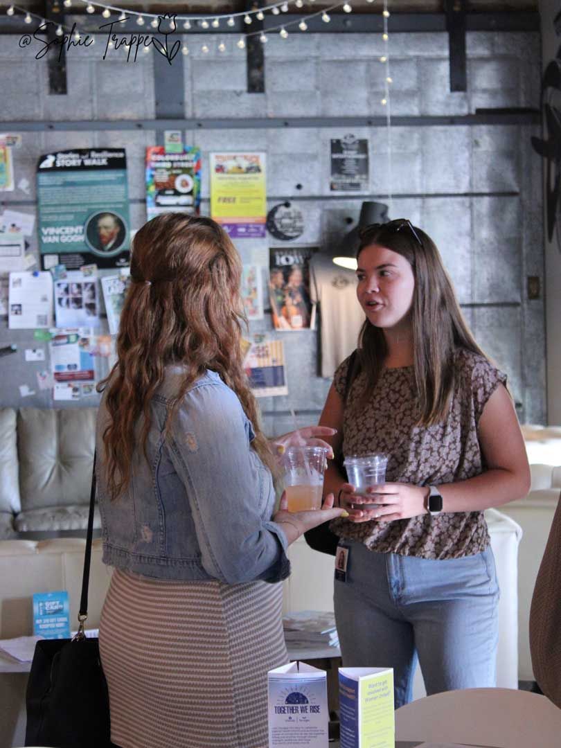 Two people talking at a table in a casual indoor setting with posters and string lights on the wall