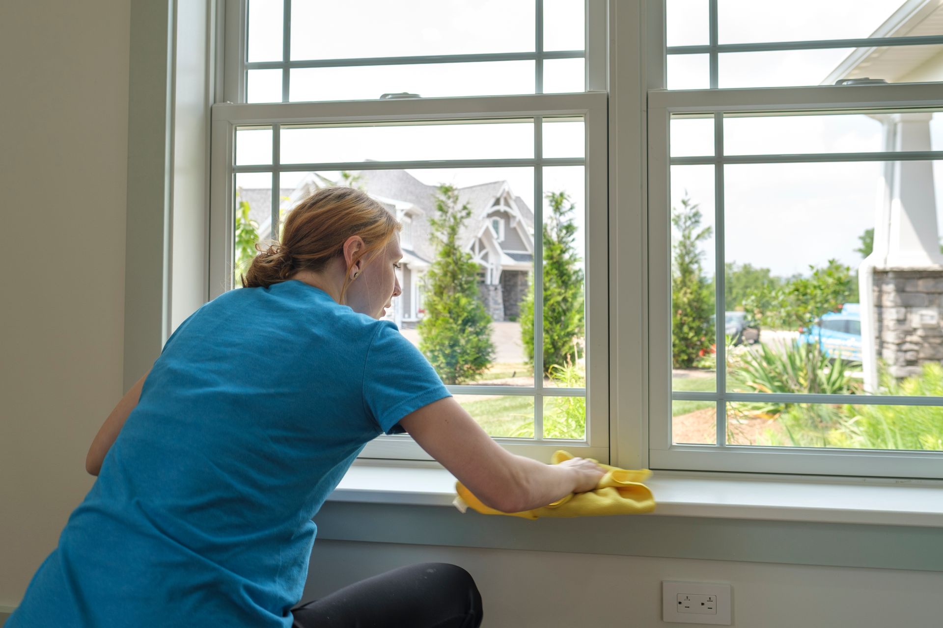 Woman in blue shirt cleaning window trim with yellow cloth.