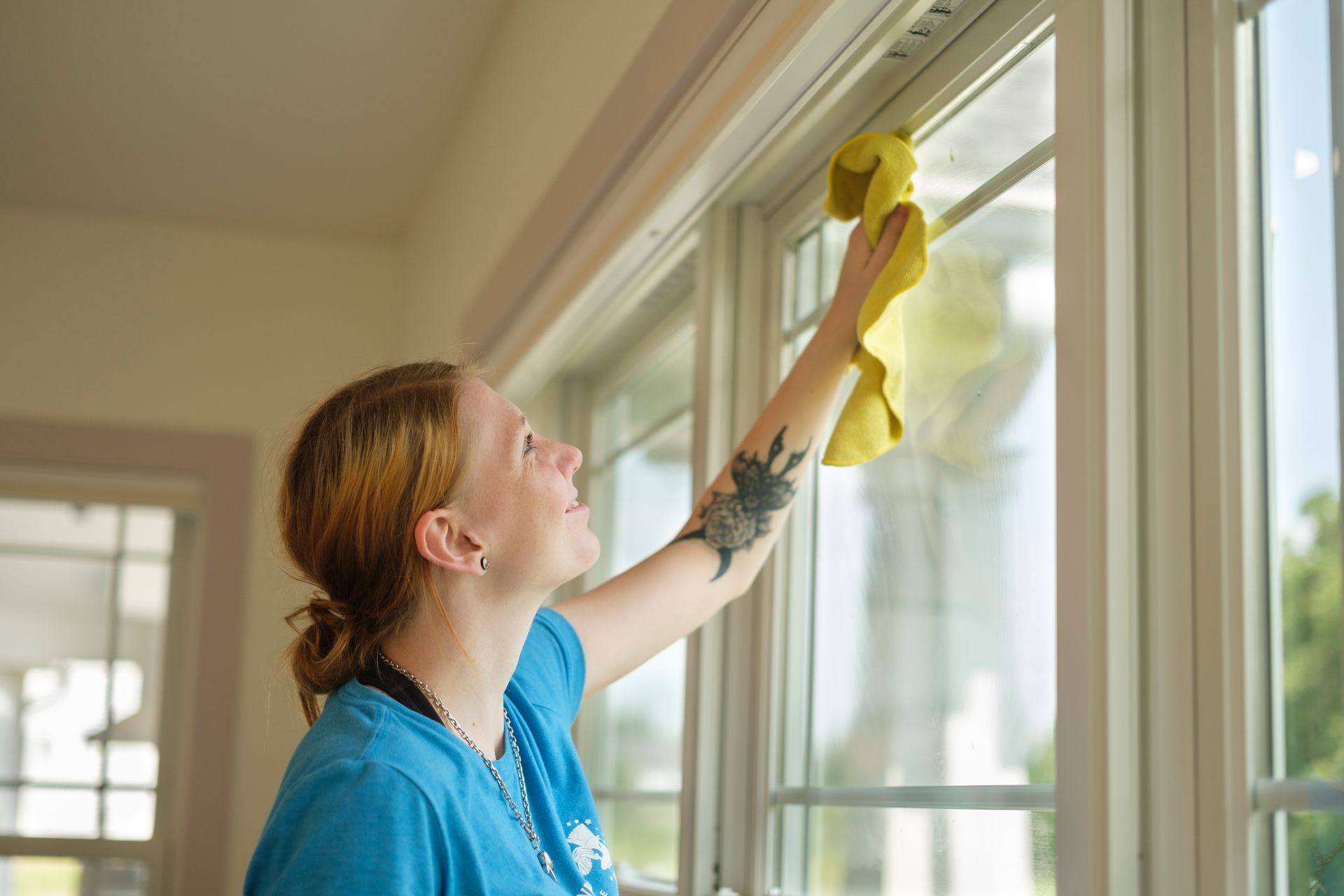 Woman cleaning a window with a yellow cloth. She is in a room with a window and a door.