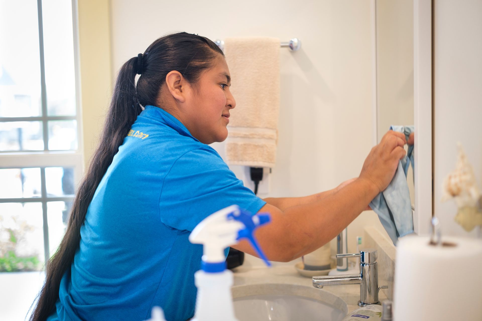 Person in blue shirt cleaning a bathroom mirror with a cloth.