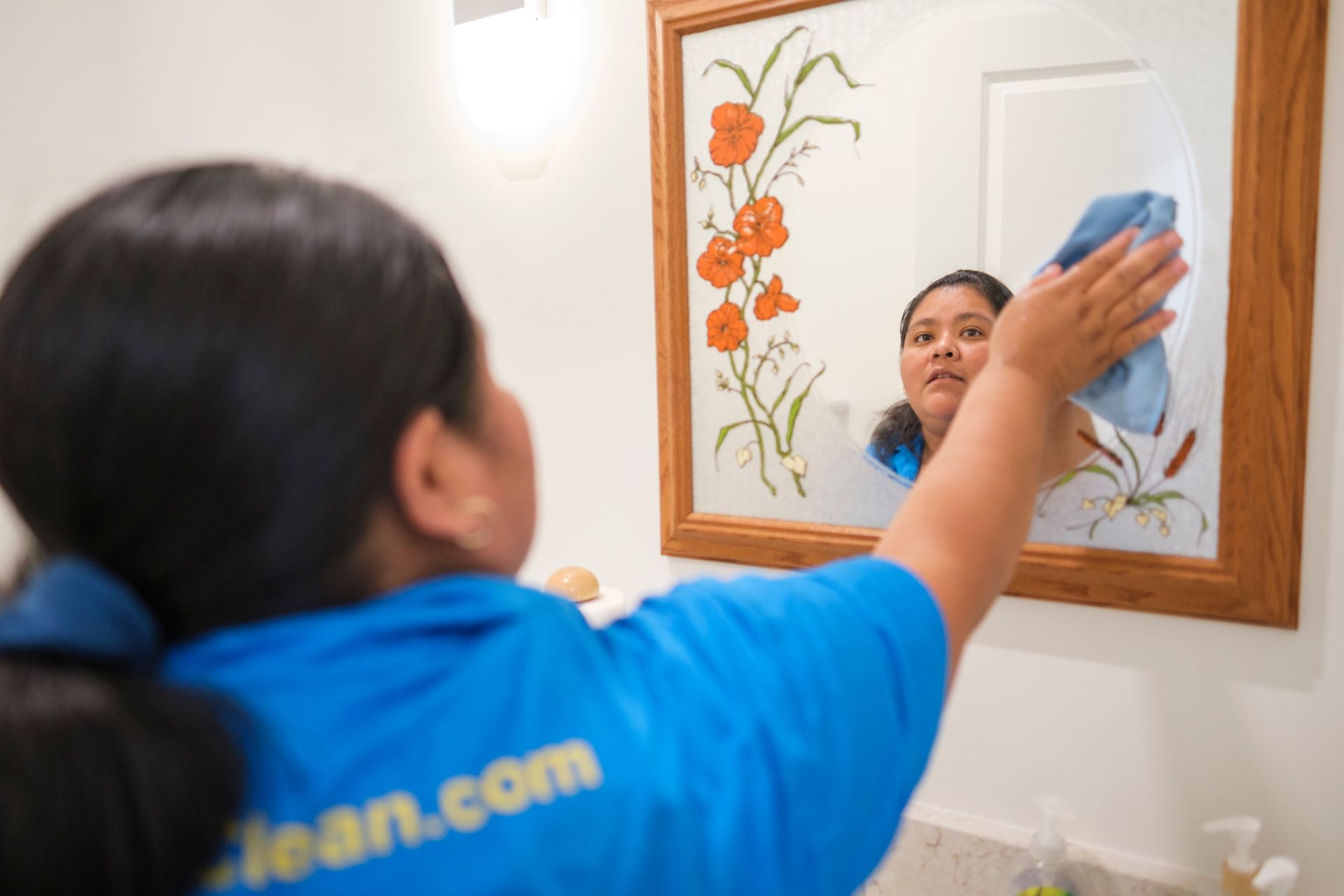 Person in blue shirt cleaning a bathroom mirror.