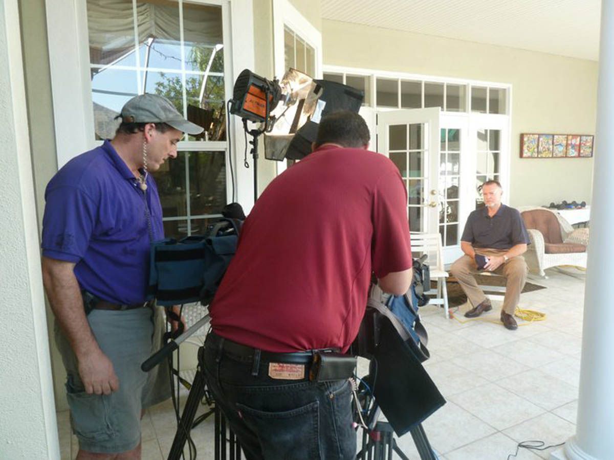 A man in a red shirt is standing in front of a camera