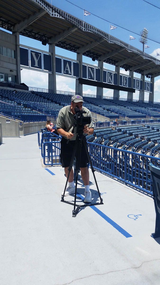 A man is standing in a stadium taking a picture with a camera.