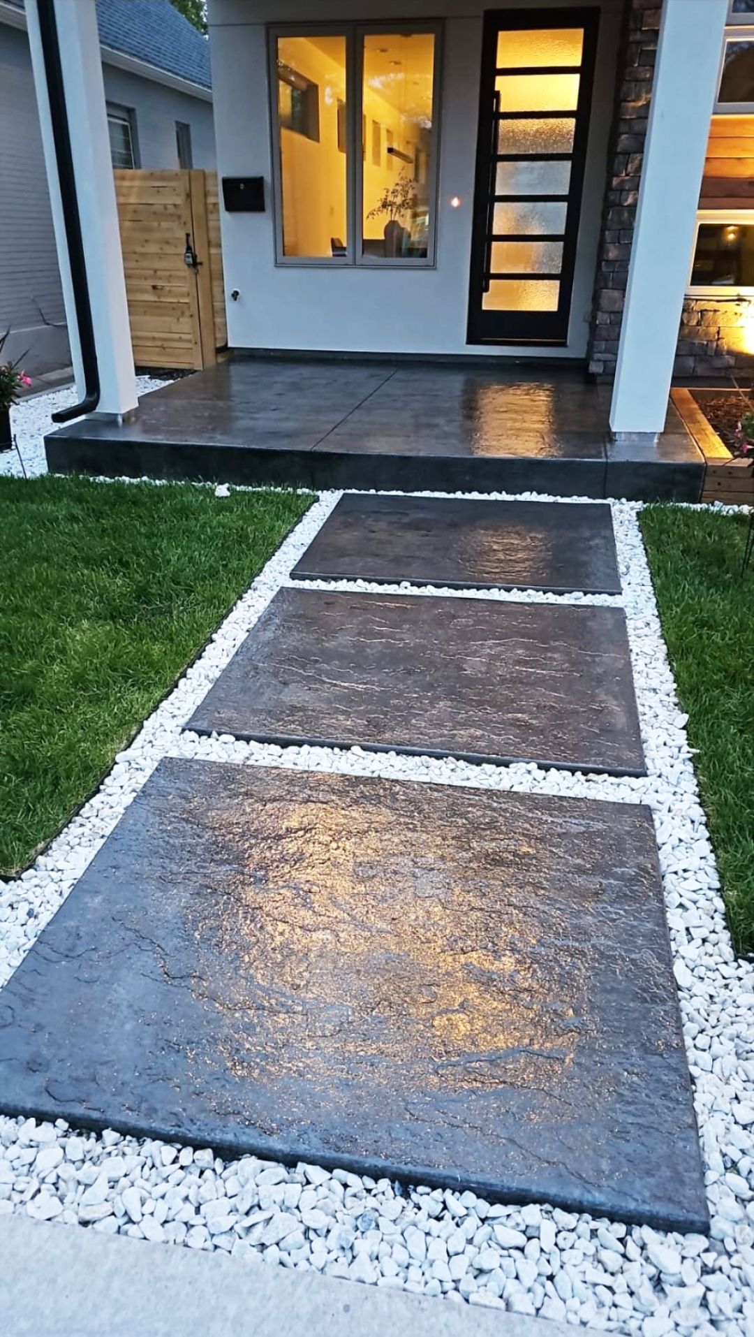 Front walkway with dark stepping stones and white gravel leading to a house entry at dusk